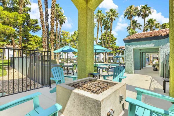 Outdoor lounge with lounge chairs, fire pit, and dining tables with umbrellas.