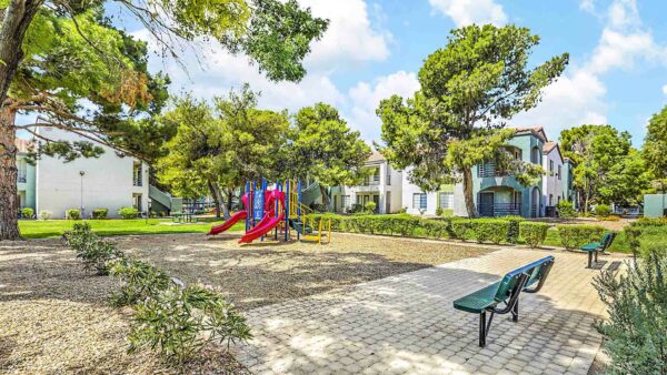 Outdoor playground with paver patio, bench seating, and lush landscaping.