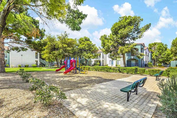 Outdoor playground with paver patio, bench seating, and lush landscaping.