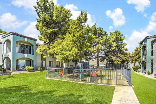 Fenced dog park with walkways, lush landscaping, and tall trees.