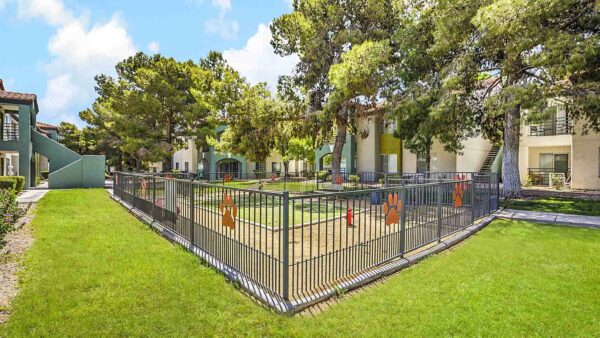 Fenced dog park with walkways, lush landscaping, and tall trees.