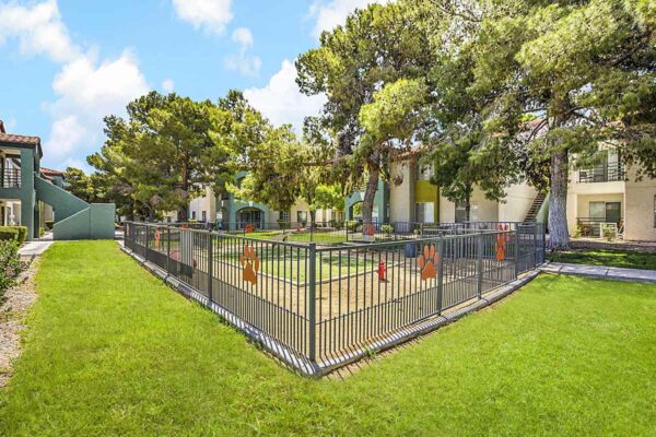 Fenced dog park with walkways, lush landscaping, and tall trees.