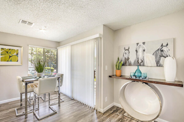 Dining room with wood floor, dining table with tall chairs, artwork, and door to balcony.