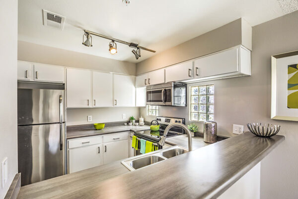 Kitchen with white cabinets, grey counters, stainless steel appliances, and glass block windows.