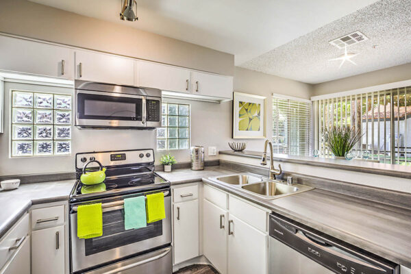 Kitchen with white cabinets, grey counters, stainless steel appliances, and glass block windows.
