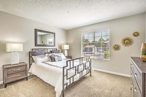 Bedroom with carpet, plush bed, bedside chests with lamps, and large window.