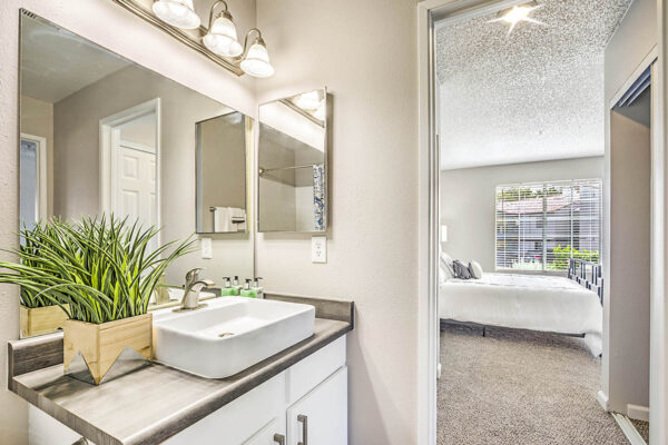 Bathroom with white cabinets, sink basin, large mirror, and door to bedroom.