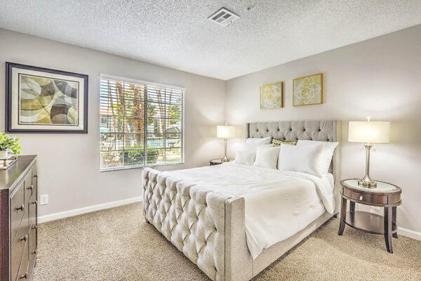 Bedroom with carpet, plush bed, bedside tables with lamps, framed art, and large window.
