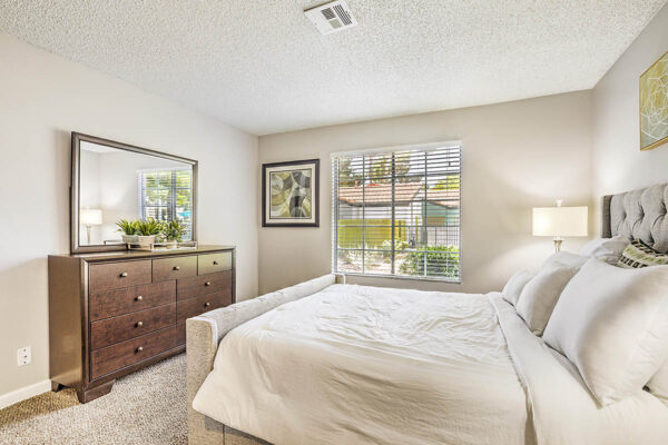 Bedroom with carpet, plush bed, dresser with mirror, framed art, and large window.
