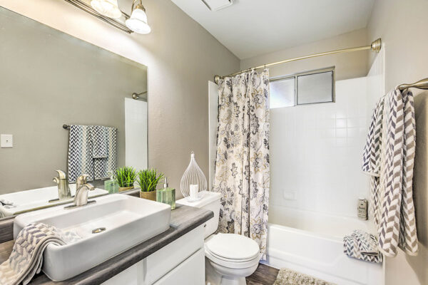 Bathroom with white cabinets, sink basin, large mirror, and tiled shower tub.