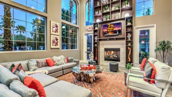 Clubhouse with plush couch, large fireplace, shelves with decor, and two story windows.