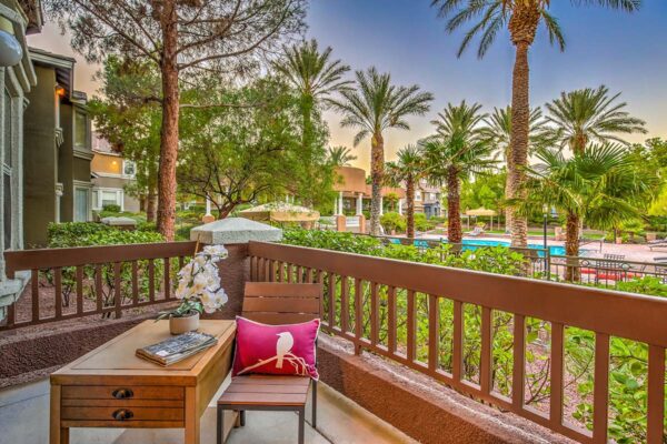 Balcony with chair and table overlooking lushly landscaped pool area with palm trees at Summerlin apartment
