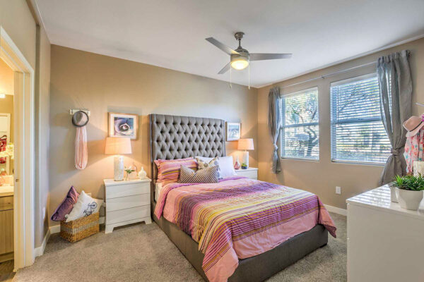 One-bedroom apartment in Summerlin with carpet, plush bed with headboard, drawers with lamps, ceiling fan, and large windows.