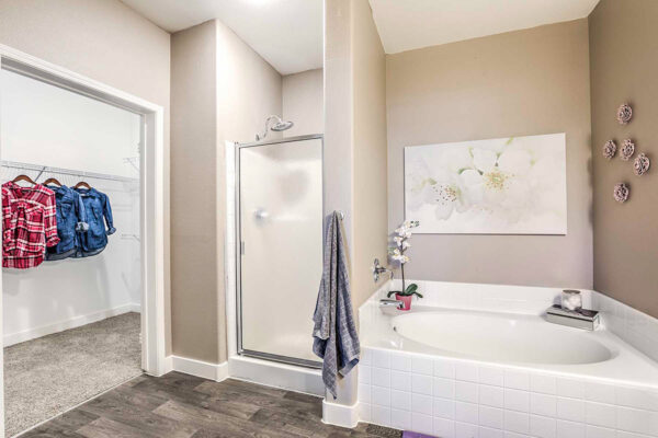 Summerlin apartment bathroom with wood floor, tiled tub and shower with glass door, artwork, and door to closet.