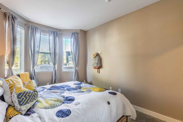 Bedroom with carpet, plush bed with bedding, and large windows with drape in Summerlin Nevada apartment