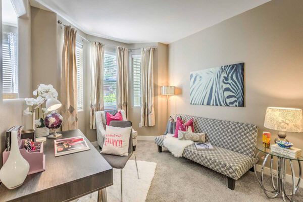 Summerlin apartment office with carpet, plush bench seat, desk with chair, and large windows.