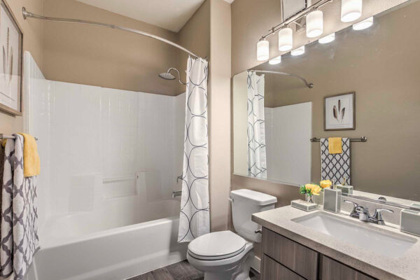 Bathroom in apartment in Summerlin with wood cabinets, light counters large mirror, and shower tub.