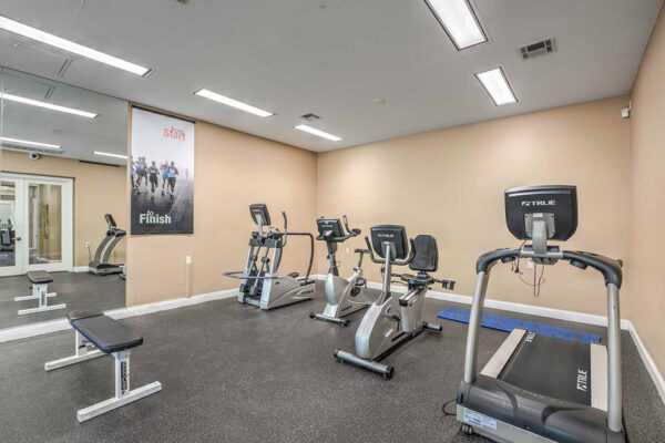 Fitness center with cardio machines, large mirror wall, and motivational poster.