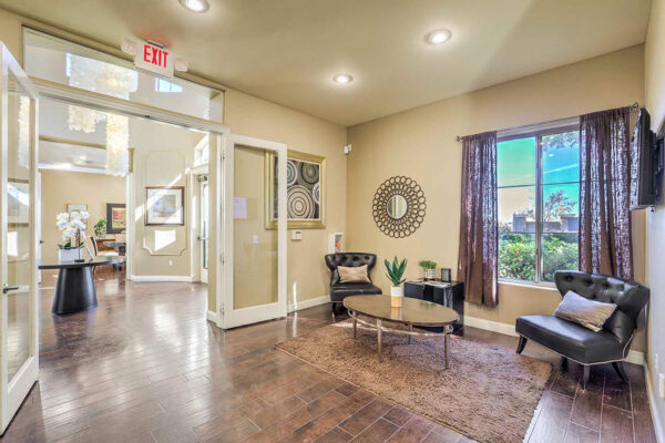 Clubroom with leather seats, tables with plants and decor, large window, and door to entry hall.
