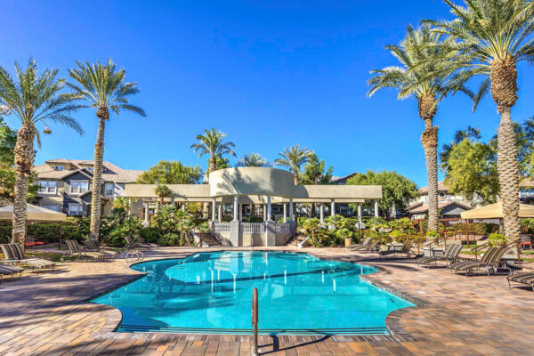 Pool area with stone paver patio, lounge chairs, gazebos, lush landscaping, and tall palm trees.