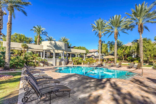 Pool area with stone paver patio, lounge chairs, gazebos, lush landscaping, and tall palm trees.