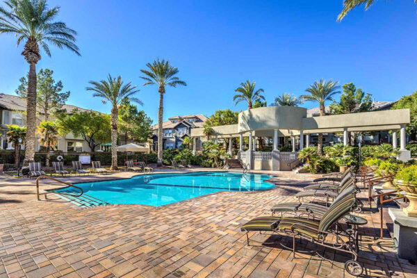 Pool area with stone paver patio, lounge chairs, gazebos, lush landscaping, and tall palm trees.