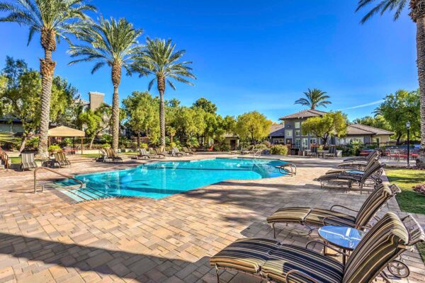Pool area with stone paver patio, lounge chairs, gazebos, lush landscaping, and tall palm trees.