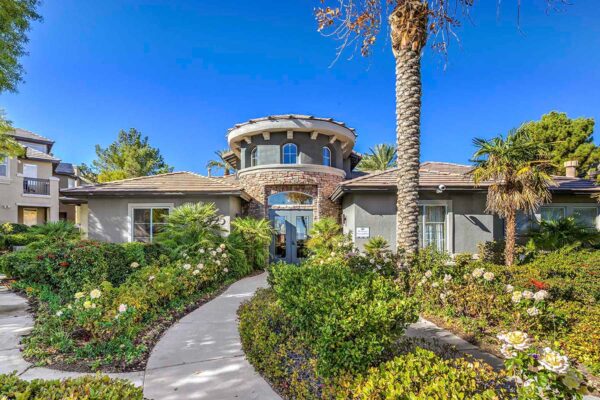 Tuscany apartment clubhouse with classic architecture, lush landscaping, and tall palm trees.