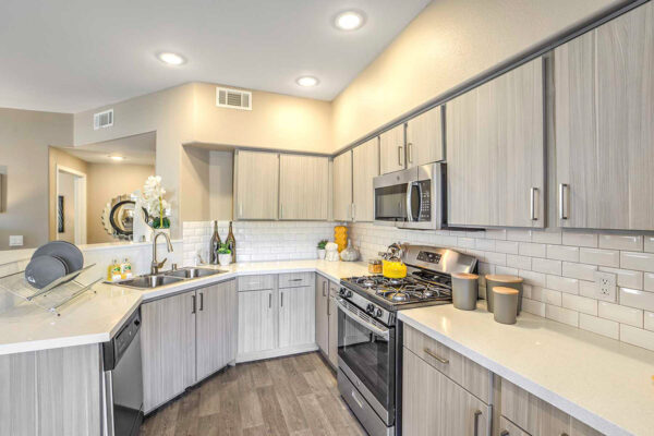 galley kitchen in apartment in Summerlin with wood floor and cabinets, light counters, stainless steel appliances, and breakfast bar.