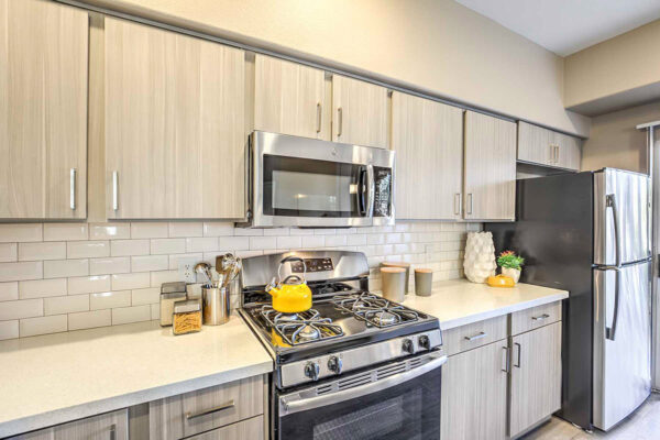 Summerlin apartment kitchen with stainless steel appliancesm, wood floor and cabinets, light counters, and colorful kitchenware.