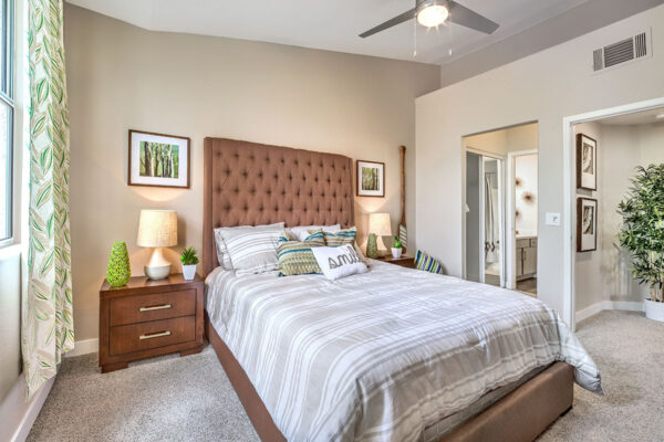 Bedroom in Summerlin apartment with en suite bathroom, carpet, plush bed and dressers with lamps and decor,