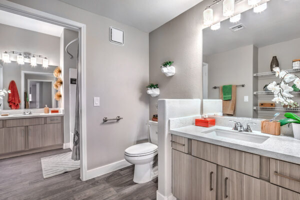 large bathroom in Summerlin apartment with wood floor and cabinets, separate counters with mirrors, and shower tub.