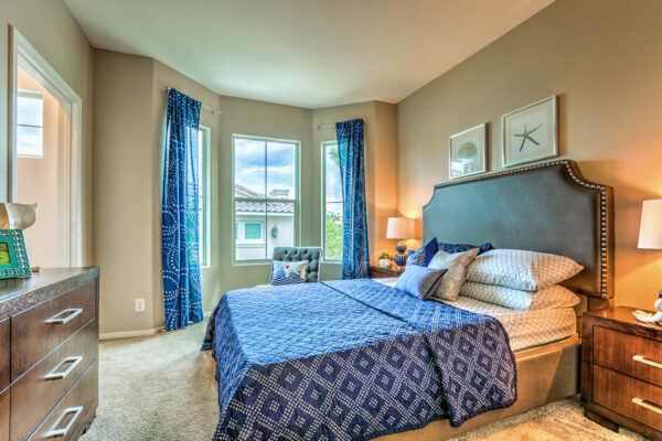 Bedroom with carpet, plush bed with headboard, bedside tables with lamps, and large windows.