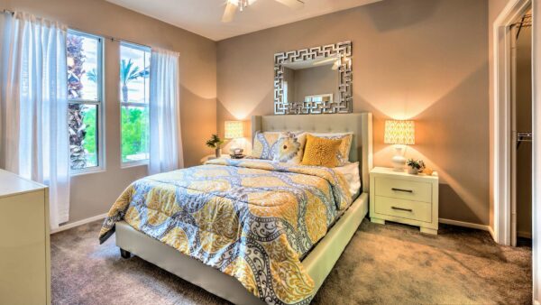 Bedroom with carpet, plush bed with headboard, bedside tables with lamps, and large windows.