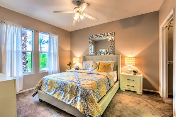 Bedroom with carpet, plush bed with headboard, bedside tables with lamps, and large windows.