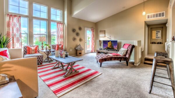 Living room with carpet, plush seating, vaulted ceilings, colorful decor, and large windows.