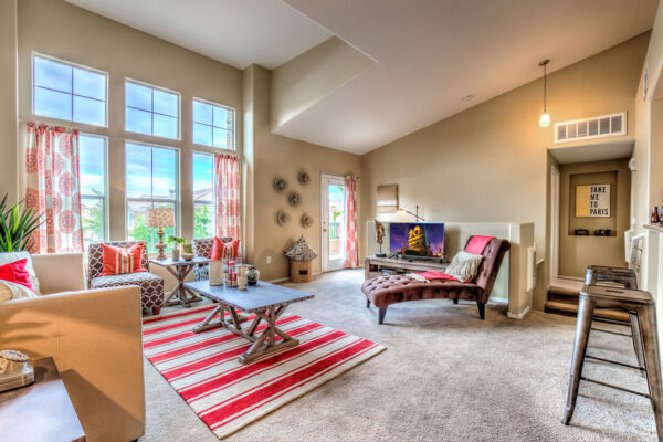 Living room with carpet, plush seating, vaulted ceilings, colorful decor, and large windows.