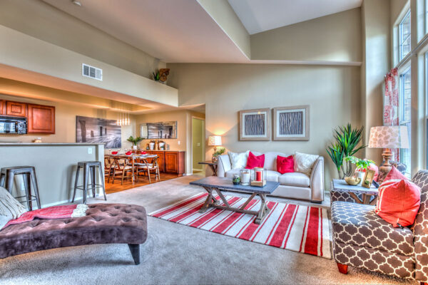 Living room with vaulted ceilings, large windows, plush carpet, and comfortable seating.