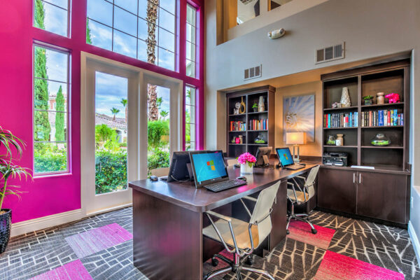 Business center with computer desks, modern chairs, large windows, and shelves with decor.
