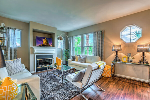Living room with plush seating, glass tables, fireplace, TV, and large windows.