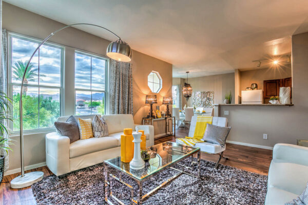 Living room with plush seating, glass tables, large lamp, eclectic decor, and large windows.