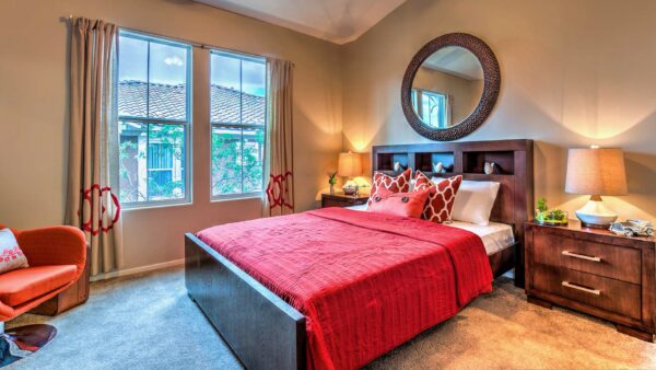 Bedroom with carpet, plush bed with headboard, bedside tables with lamps, and large windows.