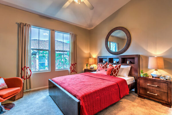Bedroom with carpet, plush bed with headboard, bedside tables with lamps, and large windows.