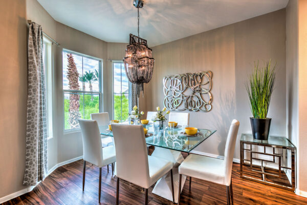 Dining room with wood floor, glass dining table with chairs, chandelier, and large windows.