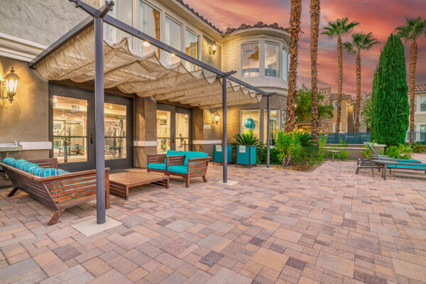 Pool area with stone paver patio, lounge chairs, tables, and pergola.