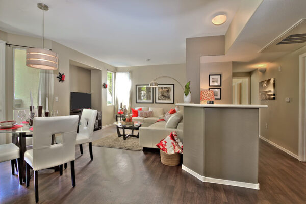 View of the open living and dining space with white furniture and dark hardwood floors.