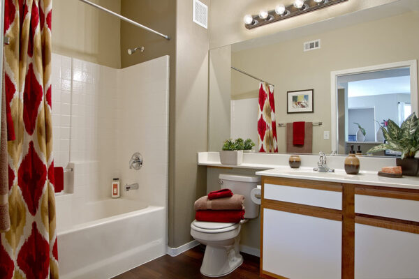 Bathroom with a white tub/shower, dark wood vanity, large mirror, and red patterned shower curtain.