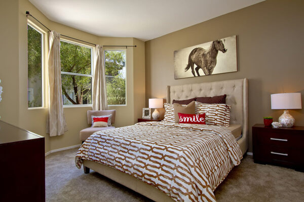 Bedroom with a tufted headboard, patterned bedding, dark wood nightstands, and a horse painting.