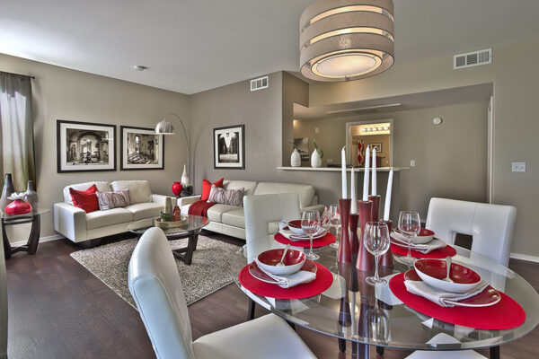 Open-plan living and dining area with white furniture, red accents, and a glass dining table.
