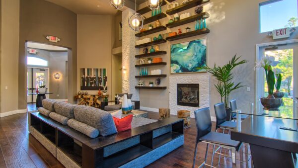 Clubhouse with plush seating, large fireplace, shelves with decor, and two story windows.